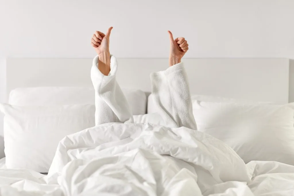 Twee duimen omhoog onder een wit dekbed